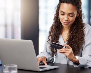 A woman online shopping on her laptop while holding her credit card.