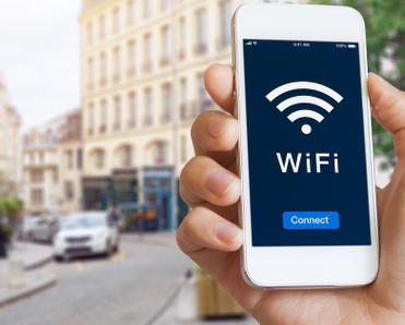 A hand holding a smartphone on a busy city street. The phone screen shows an oversized Wi-Fi signal.