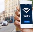 A hand holding a smartphone on a busy city street. The phone screen shows an oversized Wi-Fi signal.