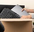 Woman placing an old laptop and keyboard in a cardboard box for recycling. 