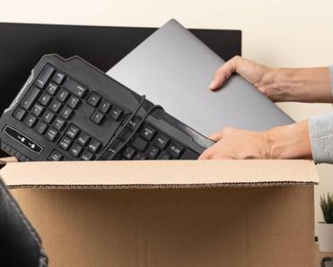 Woman placing an old laptop and keyboard in a cardboard box for recycling. 