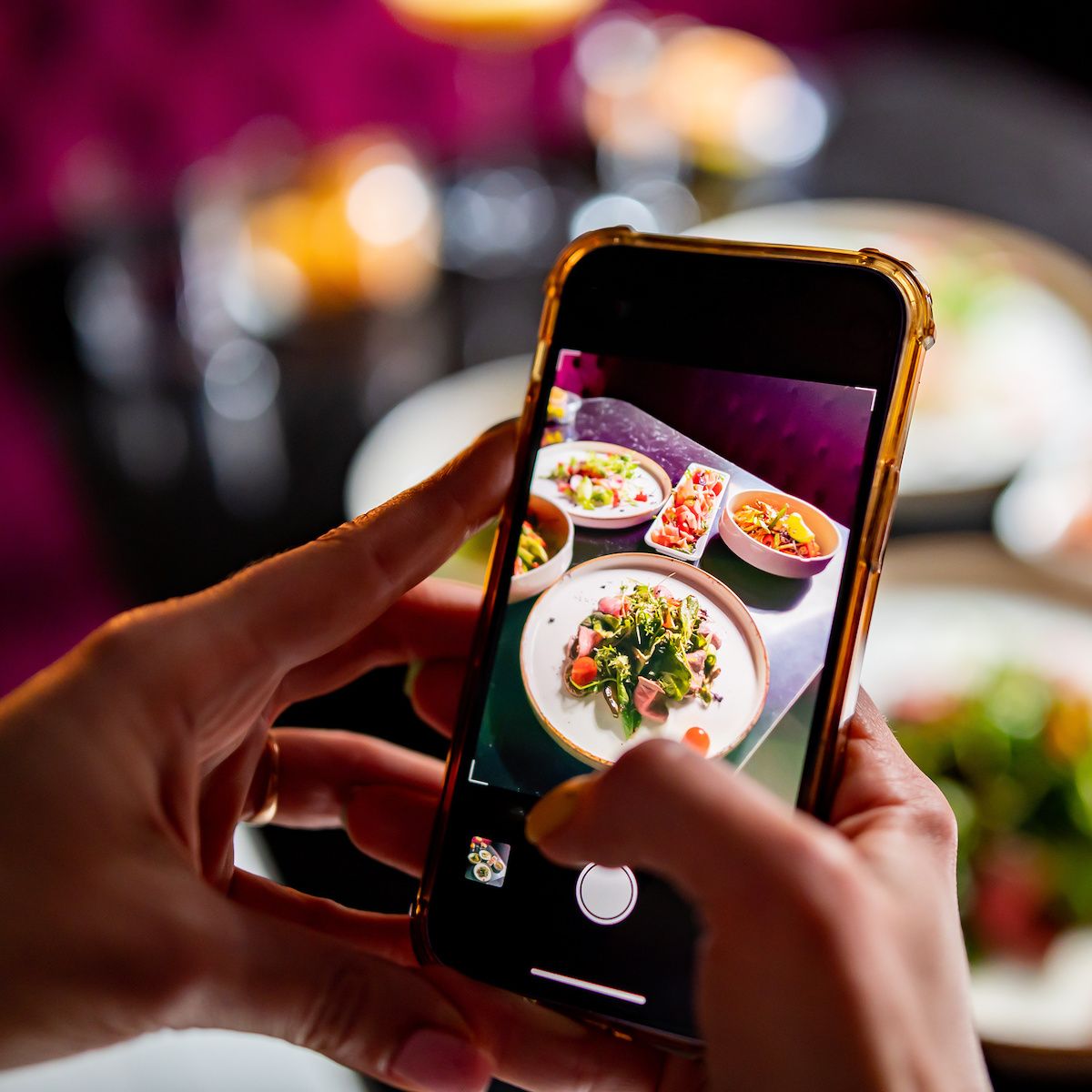 A closeup of a person holding their cell phone to take a photo of food at a restaurant.