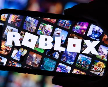 Cellphone held my hand in the dark, screen with many squares game images and the word ROBLOX across