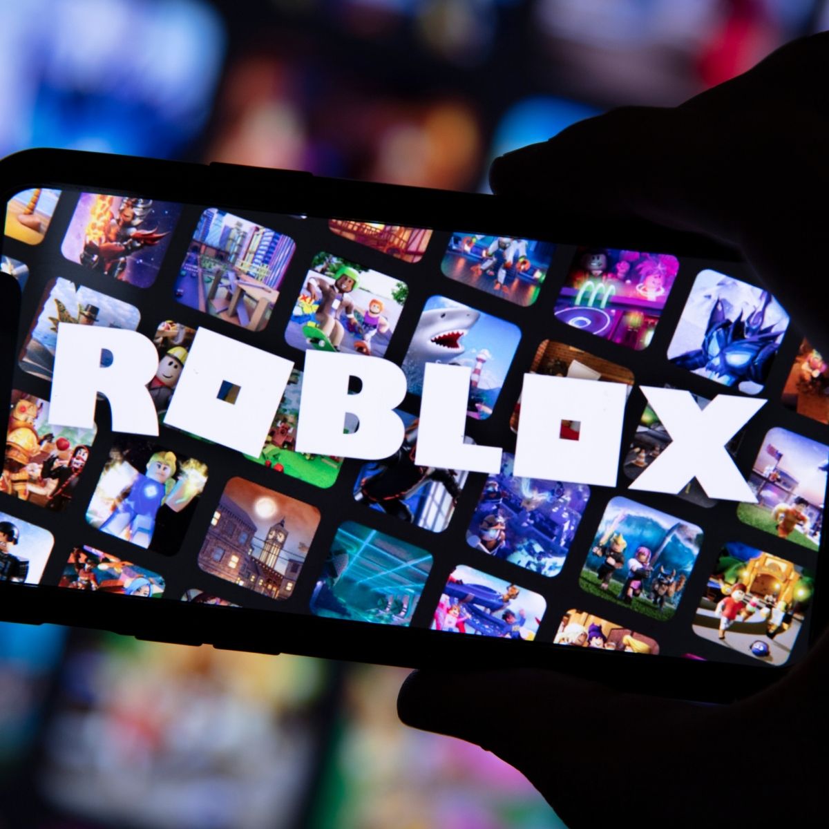 Cellphone held my hand in the dark, screen with many squares game images and the word ROBLOX across