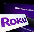 Roku purple logo on phone screen and in the back on TV 