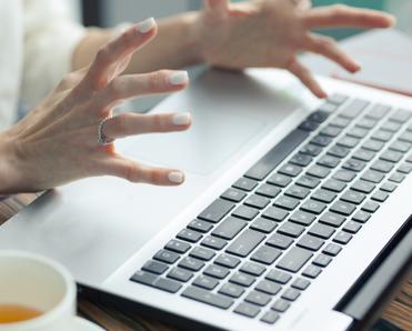 A close-up photo of a woman&#x27;s tensed hands raised above her laptop keyboard to signify a slow computer