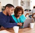 A middle-aged black man helps his older mother use social media safety tips on their home computer.