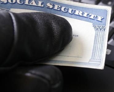 gloved hand holding social security card by computer keyboard