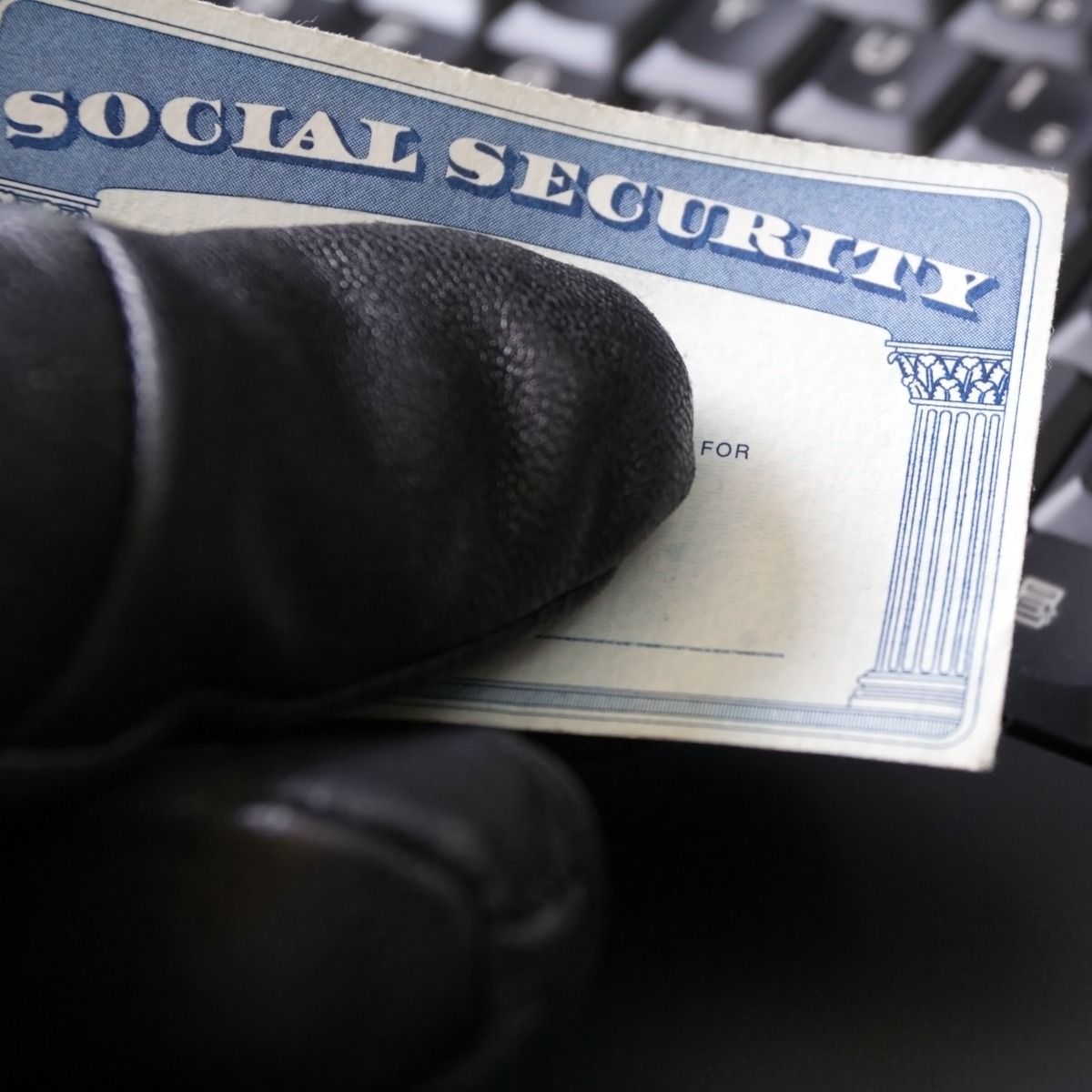 gloved hand holding social security card by computer keyboard