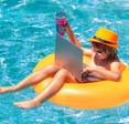 A little boy sits on a yellow floatation device in a swimming pool while using a laptop.