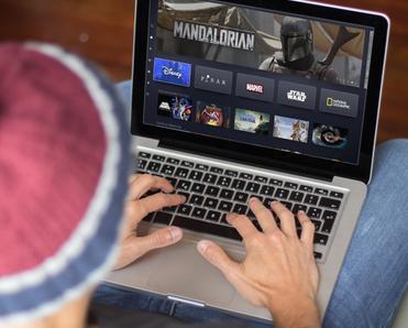 man wearing beanie typing on laptop keyboard while &quot;The Mandalorian&quot; and streaming shows on screen