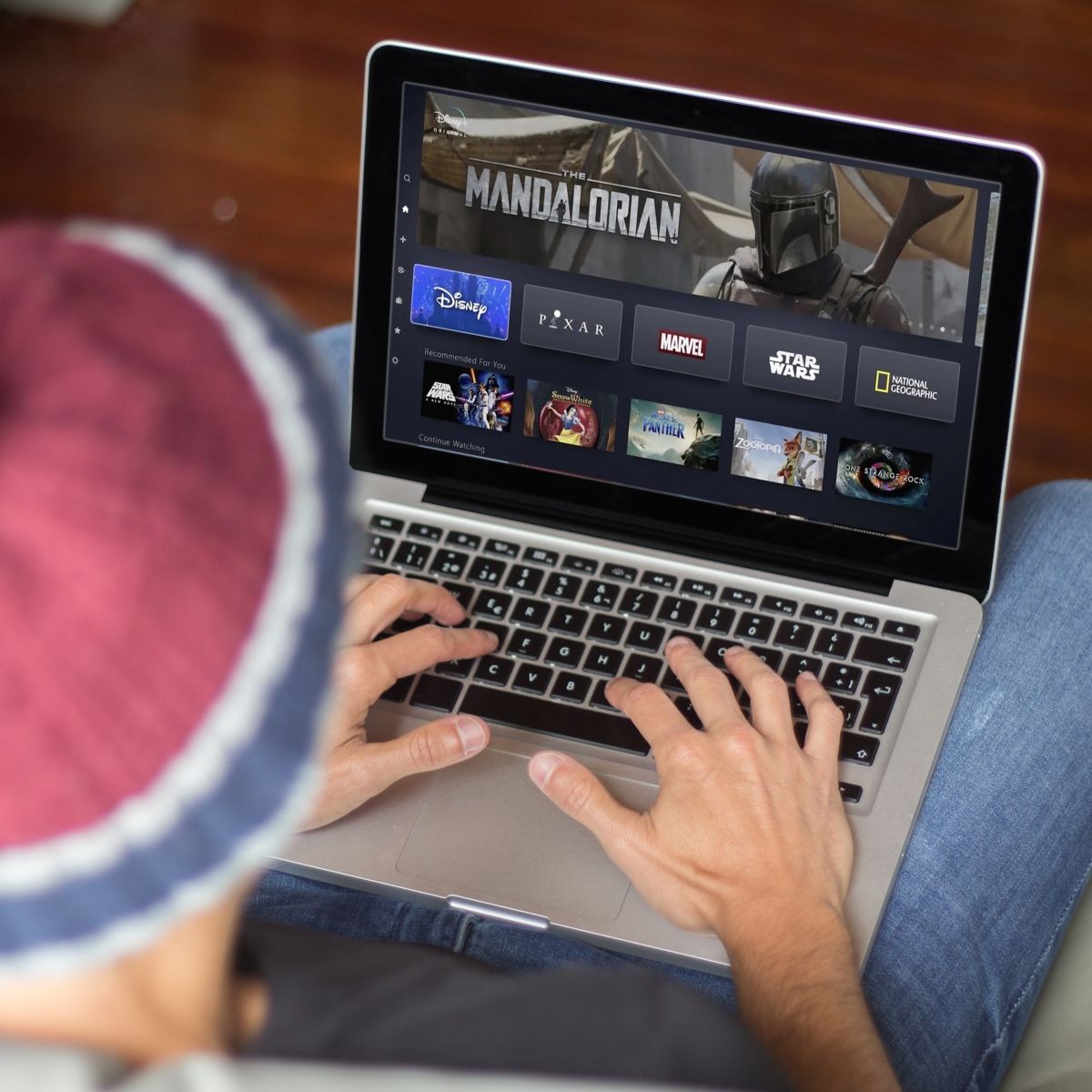 man wearing beanie typing on laptop keyboard while &quot;The Mandalorian&quot; and streaming shows on screen