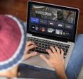 man wearing beanie typing on laptop keyboard while &quot;The Mandalorian&quot; and streaming shows on screen