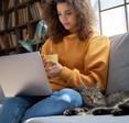A young woman sits on a sofa with her pet cat and watches a TV show on her laptop. VPNs can help you unblock foreign streaming content.