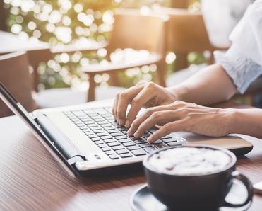 A woman&#x27;s hands rest on a laptop keyboard while she sits in a coffee shop. Using unsecure public Wi-Fi could put you at risk for a man-in-the-middle attack.