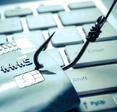 A credit card is captured with a fish hook on top of a laptop, indicating the card information is going to be stolen.