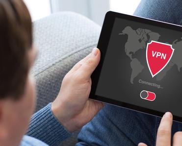 A man holds a tablet that shows a VPN with a red shield logo connecting to a server.