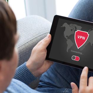 A man holds a tablet that shows a VPN with a red shield logo connecting to a server.