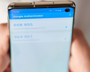 Two hands hold an Android smartphone with the Google Authenticator app open.