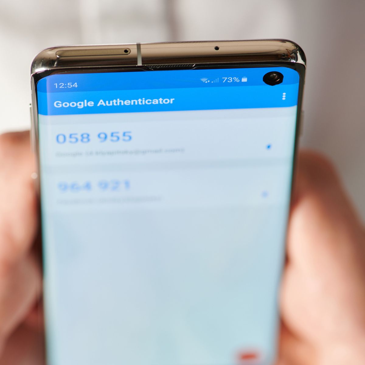 Two hands hold an Android smartphone with the Google Authenticator app open.
