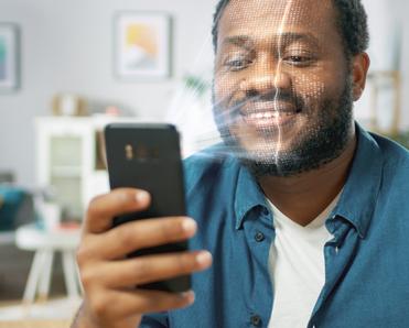 A young bearded Black man holds his cell phone in front of his face with an illustration of the phone&#x27;s camera scanning his face so he can log into his phone using facial recognition