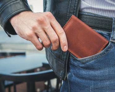 A man pulls a brown leather wallet out of his pocket. Some people claim RFID wallets are necessary to prevent RFID fraud, but is that really true?