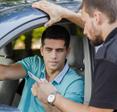 A young man showing his driver&#x27;s license and vehicle documentation to a cop from his car.