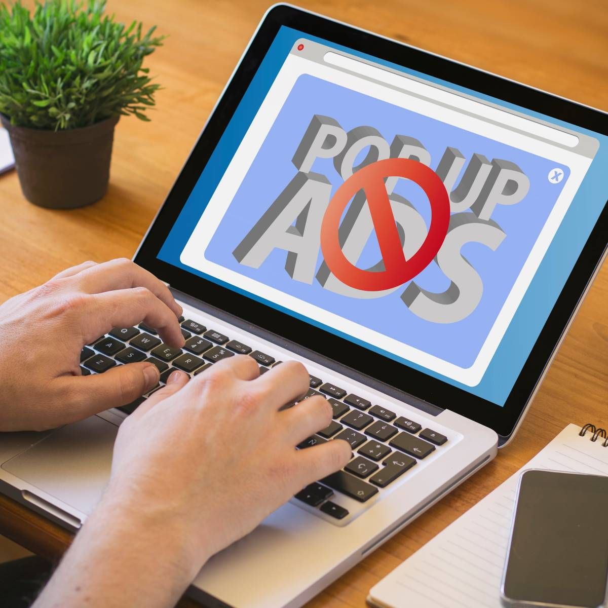 A person using a laptop with a screen showing a pop-up ad being blocked.