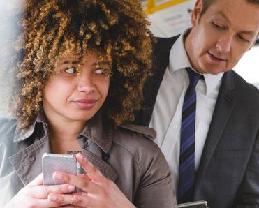 A man is peeking over a woman&#x27;s shoulder at her phone while they are on a bus.