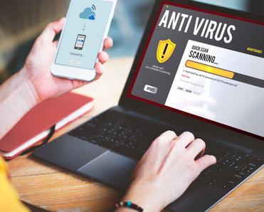 A woman&#x27;s hands hold her cell phone and type on her laptop while an antivirus software scan is on the screen