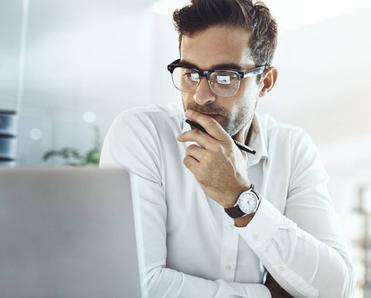 A businessman in an office staring at his computer and thinking.