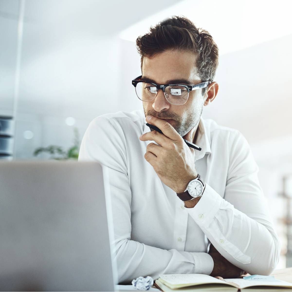 A businessman in an office staring at his computer and thinking.