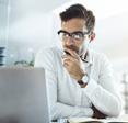 A businessman in an office staring at his computer and thinking.