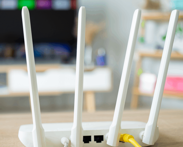 A close-up photo of the back of a white wireless router placed on a table, a yellow Ethernet cable is plugged into the back.