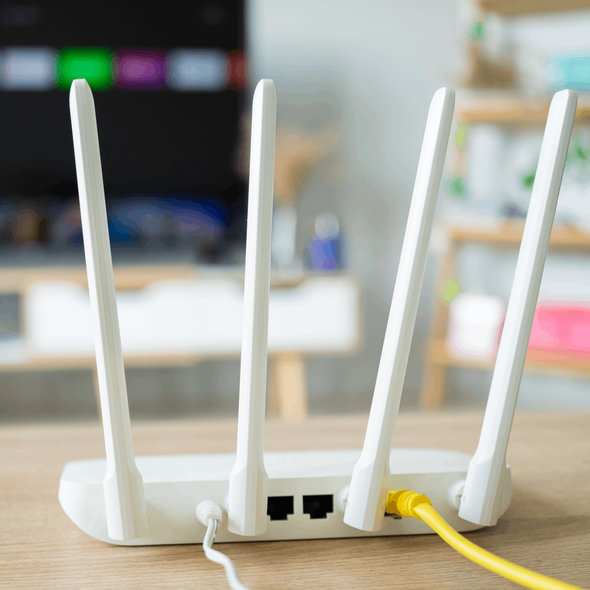 A close-up photo of the back of a white wireless router placed on a table, a yellow Ethernet cable is plugged into the back.