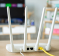 A close-up photo of the back of a white wireless router placed on a table, a yellow Ethernet cable is plugged into the back.